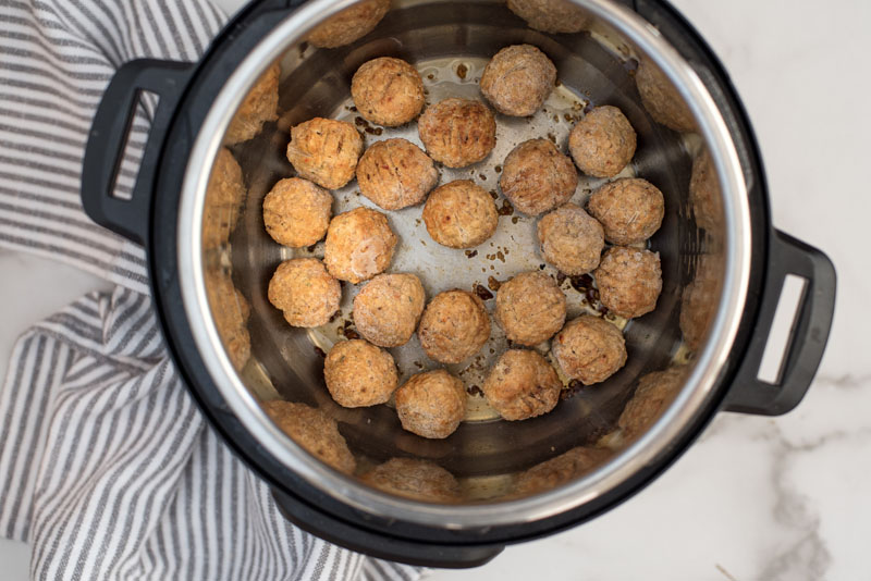 overhead of an electric instant pot pressure cooker with frozen meatballs being sauteed for spaghetti and meatballs