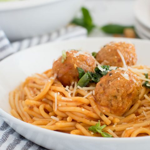 Close up on a white pasta bowl filled with instant pot spaghetti and meatballs with grated parmesan cheese and fresh parsley