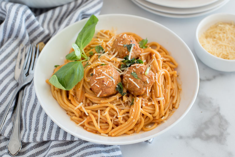 Close up of white bowl with spaghetti and meatballs, spaghetti sauce and fresh basil leaves