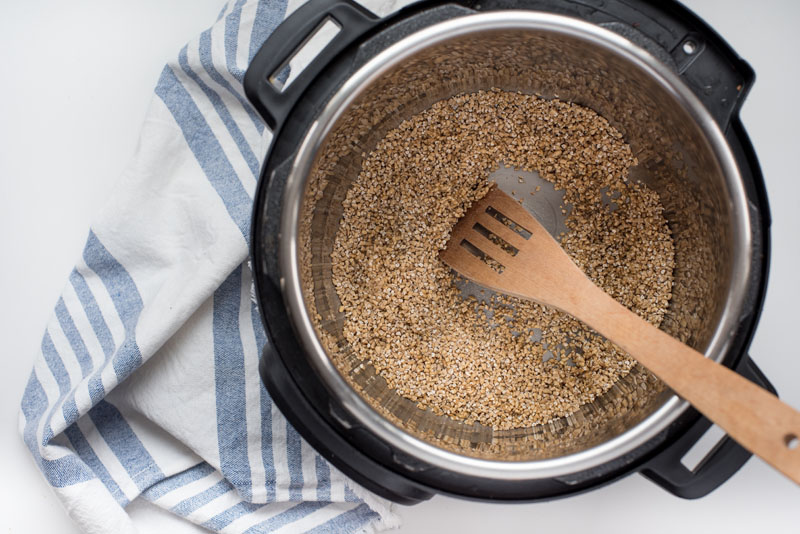 instant pot with dry steel cut oats being toasted in butter with a wooden stirring spoon