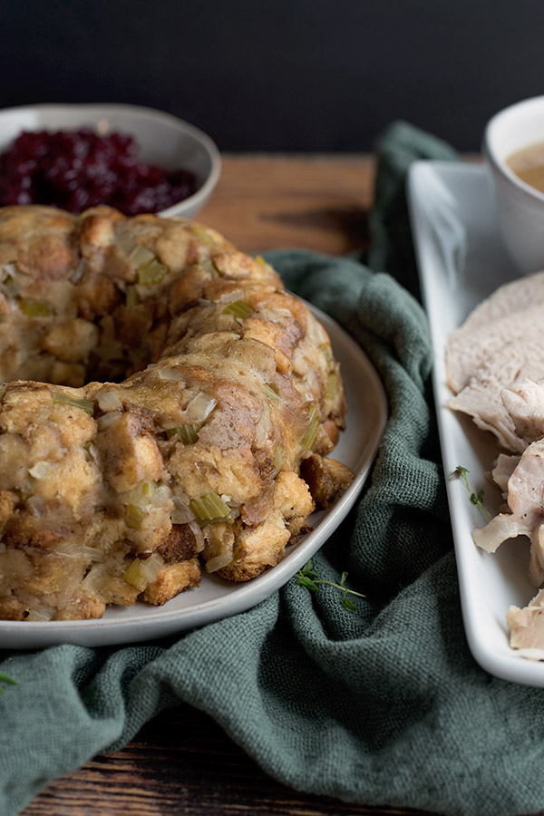 Bread stuffing on a plate, next to a plate of turkey and a bowl of cranberry sauce in the background.