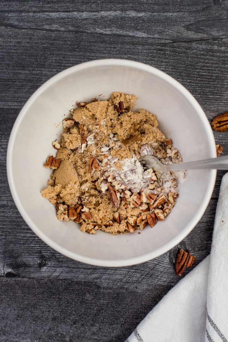 white bowl with ingredients for crumble topping - brown sugar, nuts, spices