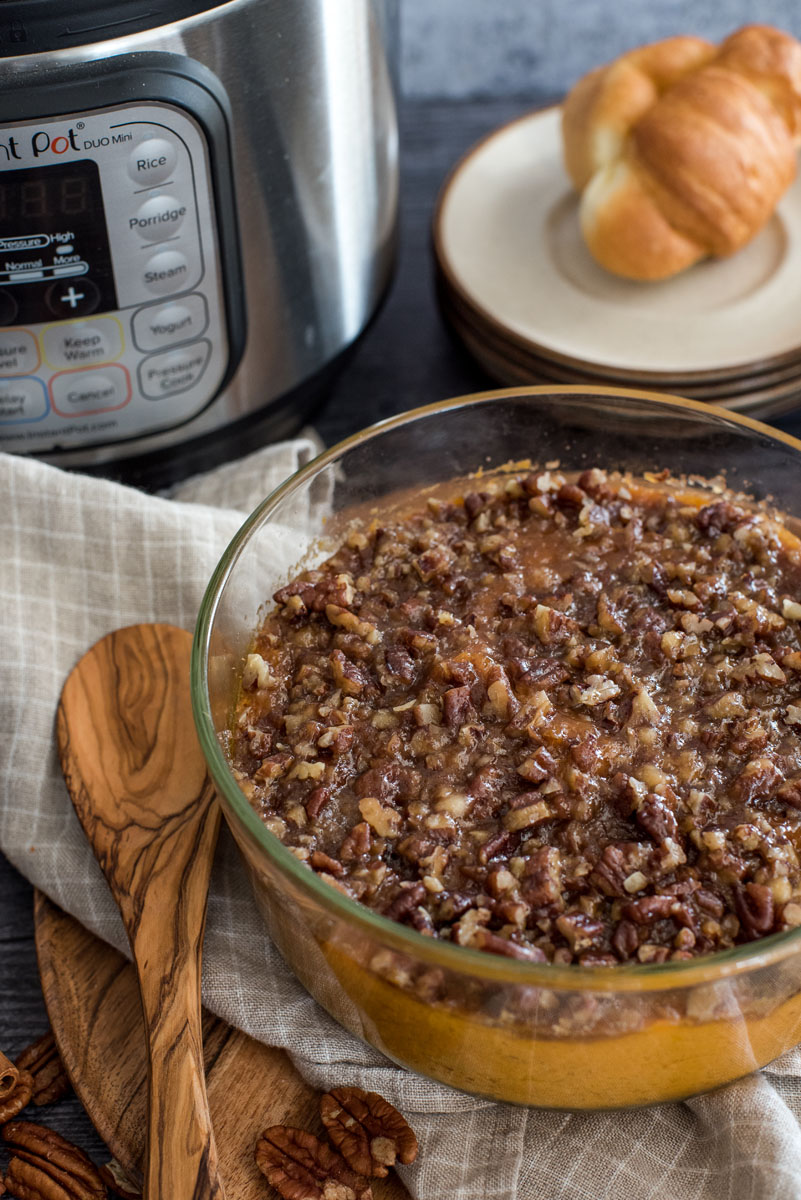 sweet potat casserole in front of an instant pot with a sooden spoon and a nutty crust