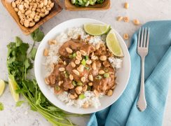 an overhead shot of Instant pot peanut thai chicken with cilantro lime sauce and white rice, with a blue napkin and a fork on it, a sprg on cilantro on the other side, and small dishes of peanuts and green onions at the top