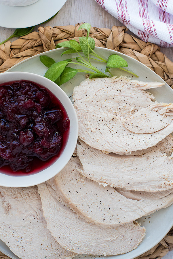 Pressure cooker turkey breast sliced and plated with fresh sage and cranberry sauce.