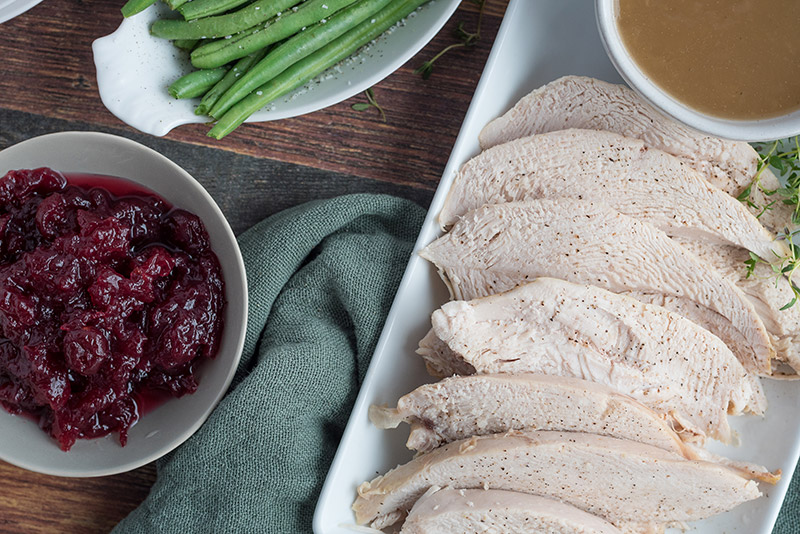Pressure cooker turkey breast sliced and plated with gravy, a bowl of cranberry, and green beans.