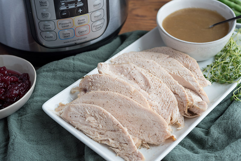 A rectangle plate of Pressure Cooker Thanksgiving Turkey recipe, with and Instant Pot, gravy, and cranberries in the background