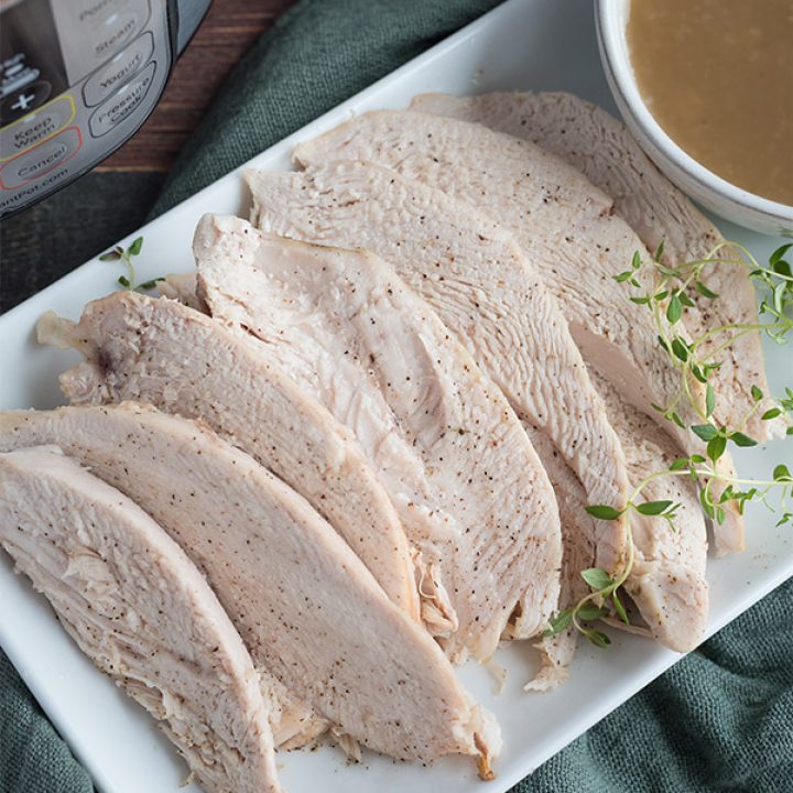 Pressure Cooker Turkey Breast cooked in the Instant Pot, sliced on a white platter with gravy and cranberries