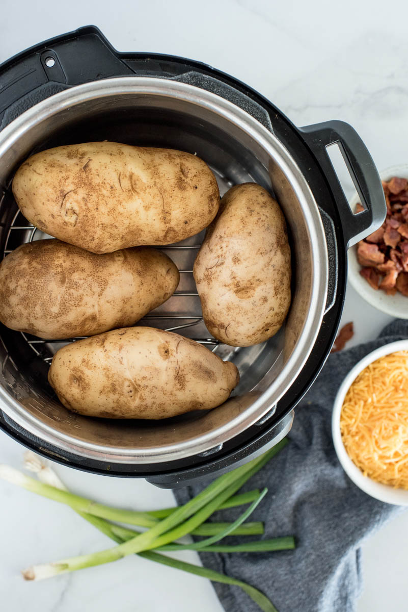 overhead of an instant pot with four russet potatoes inside on a wire rack or trivet