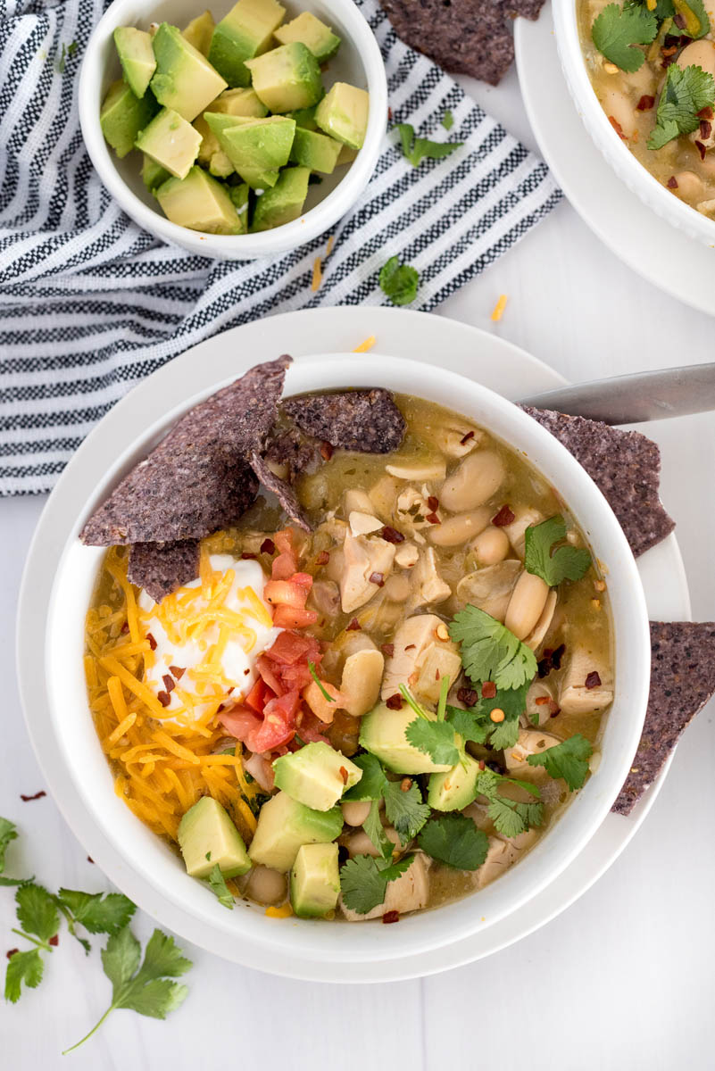 bowl of instant pot white chicken chili with avocado, chips and shredded cheese on top