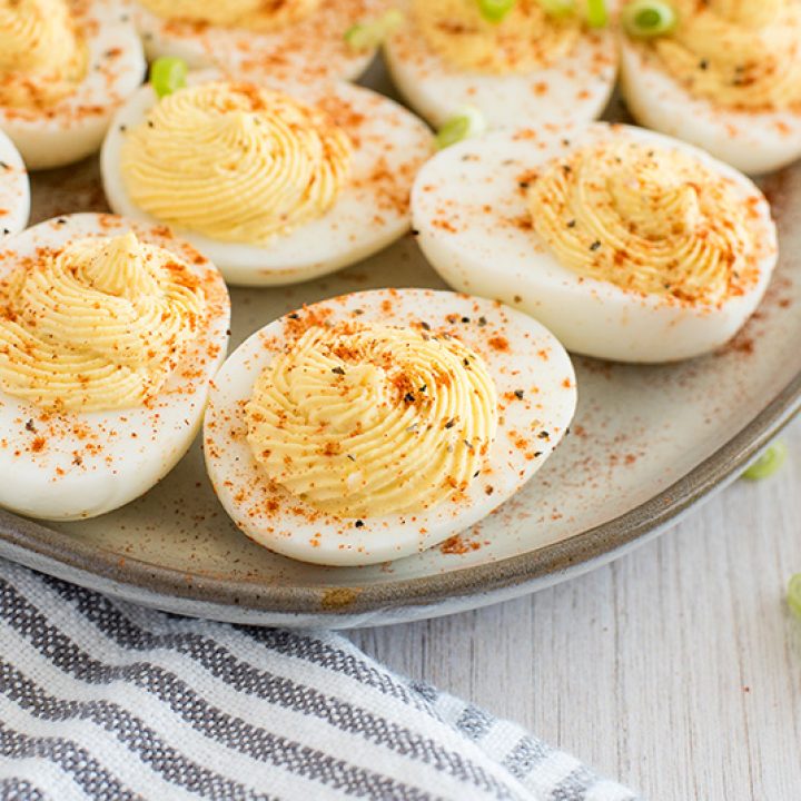 Close up on a dozen hard-boiled eggs sliced in half and filled with Instant Pot deviled egg filling made with mayonnaise, egg yolks, Greek yogurt and smoked paprika.