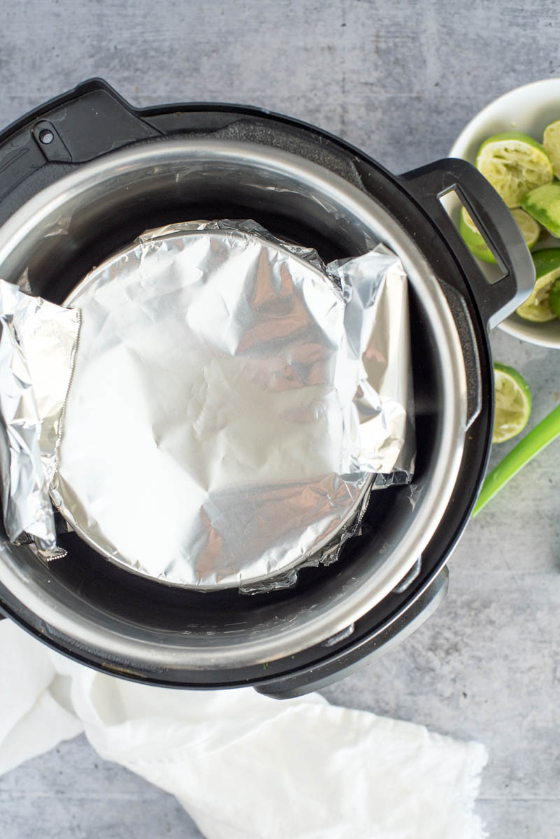 overhead of an instant pot with a covered pie lowered with a foil sling