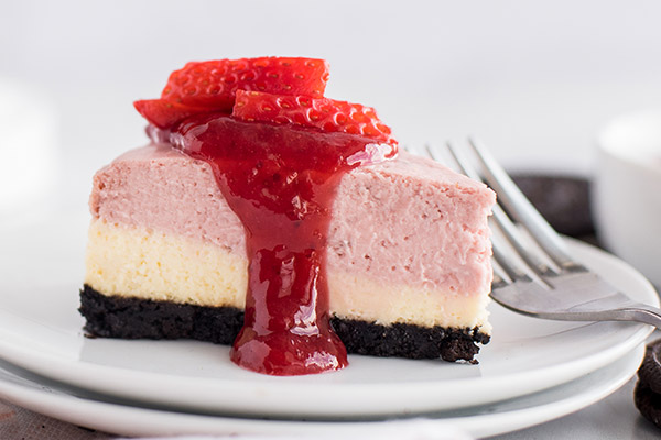 Close up of a layered strawberry cheesecake, cooked in an Instant Pot pressure cooker, garnished with a drizzle of strawberry sauce and fresh strawberries