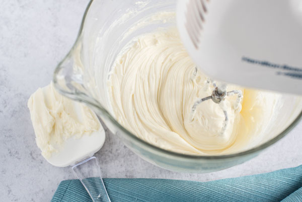 Cream cheese being mixed gently with a hand mixer