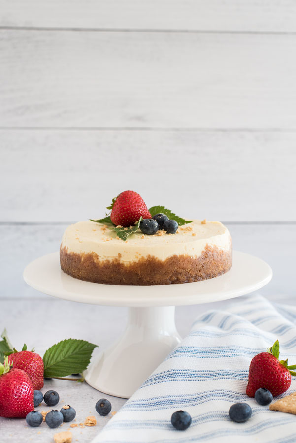 Profile view of an Instant Pot cheesecake on a cake stand, topped with berries.