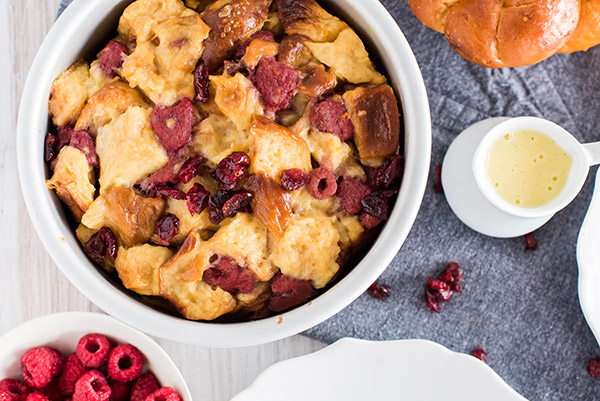 Overhead shot of Instant Pot Bread Pudding inside of the cake pan, with a bowl of raspberries and creme anglaise along the edge of the photograph