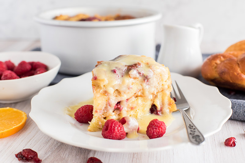 Pressure Cooker Raspberry Orange Bread Pudding, dished up with the cake pan and bowl of raspberries in the background