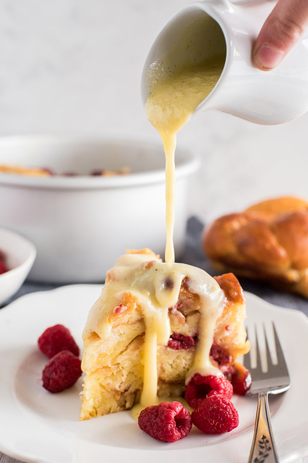 A close up of raspberry orange bread pudding  on a plate being drizzled with cream cheese frosting
