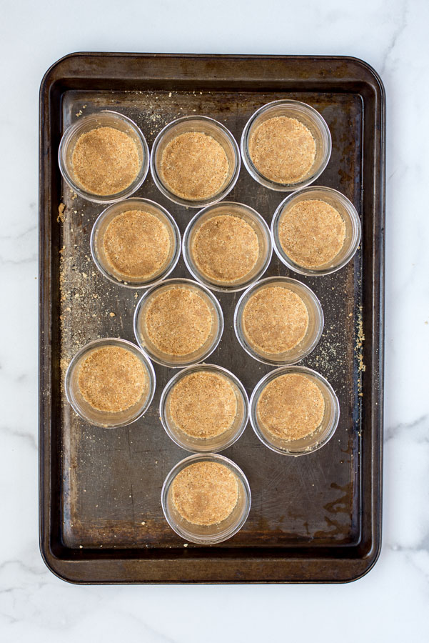 Overhead of mini mason jars with homemade graham cracker crumb crust on a metal baking sheet 