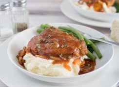 pork and gravy served on a white plate with  green beans
