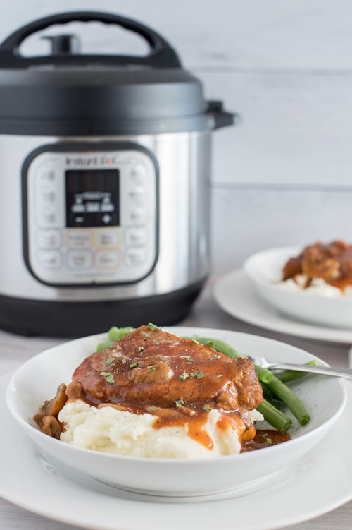 A plated serving of boneless pork chops and gravy in front of an Instant Pot