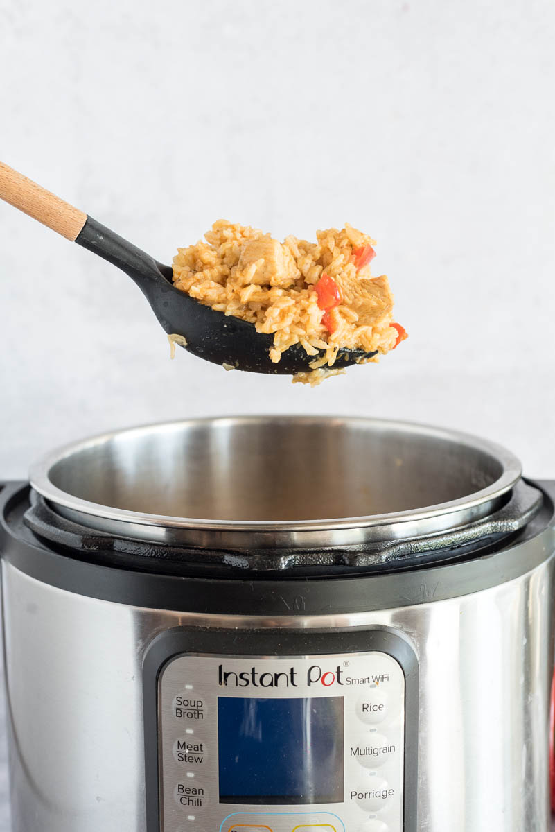 A spoon taking out a serving of Instant Pot Chicken and Rice, suspended over an Instant Pot