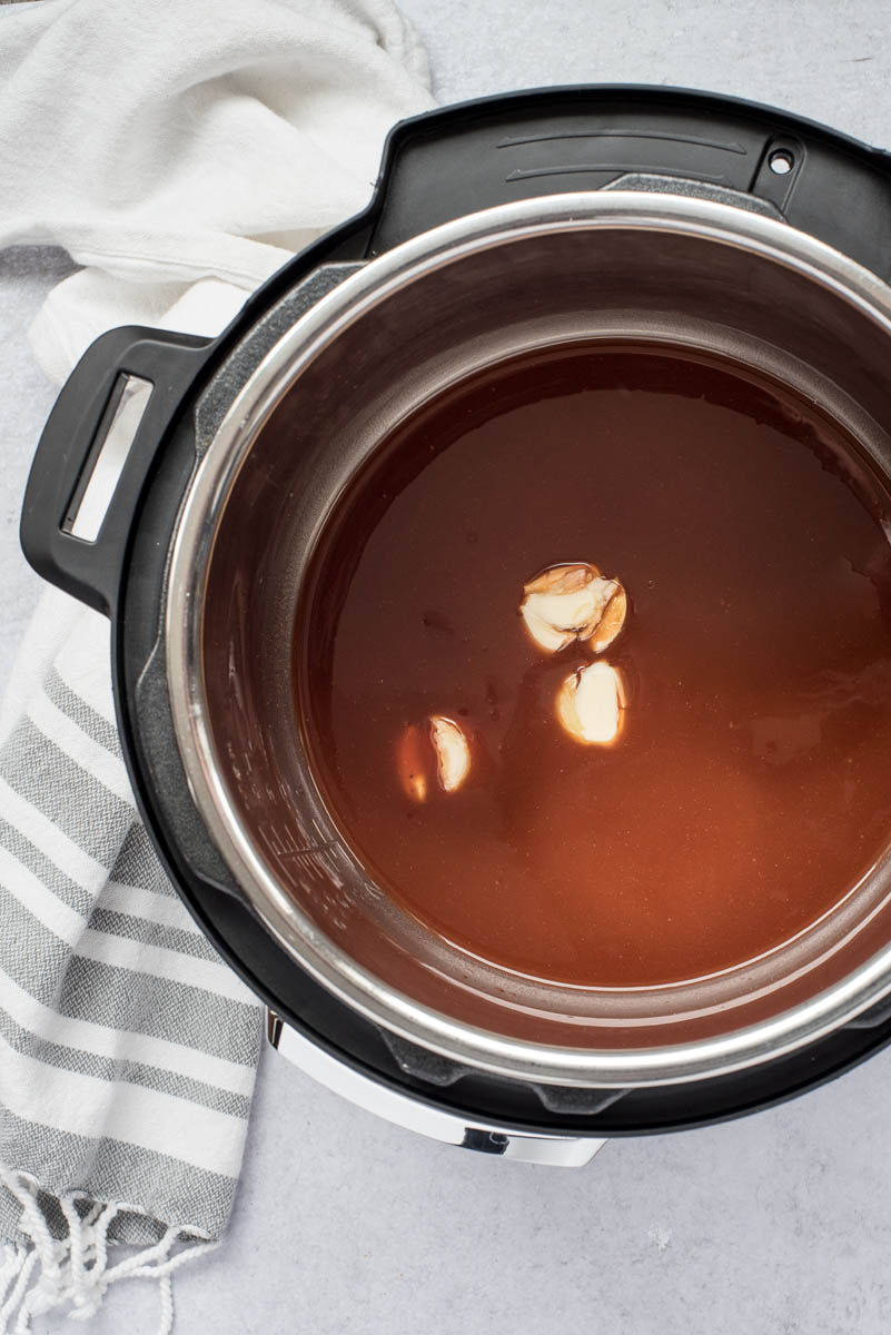 A top-down shot of BBQ sauce, liquid smoke, and smashed cloves of garlic inside the Instant Pot's cooking pot.