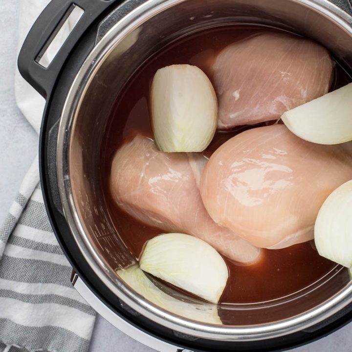 An overhead shot of three chicken breasts inside the Instant Pot with halved onions