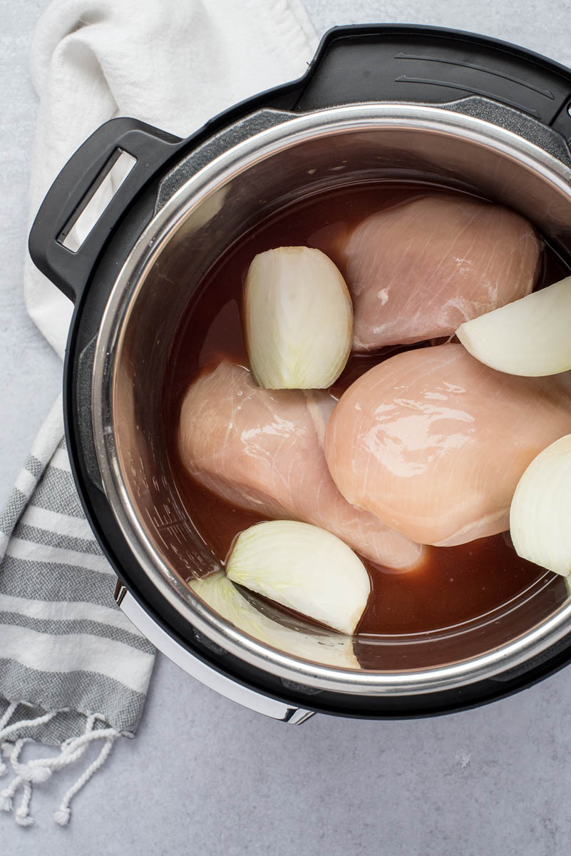 An overhead shot of three chicken breasts inside the Instant Pot with halved onions