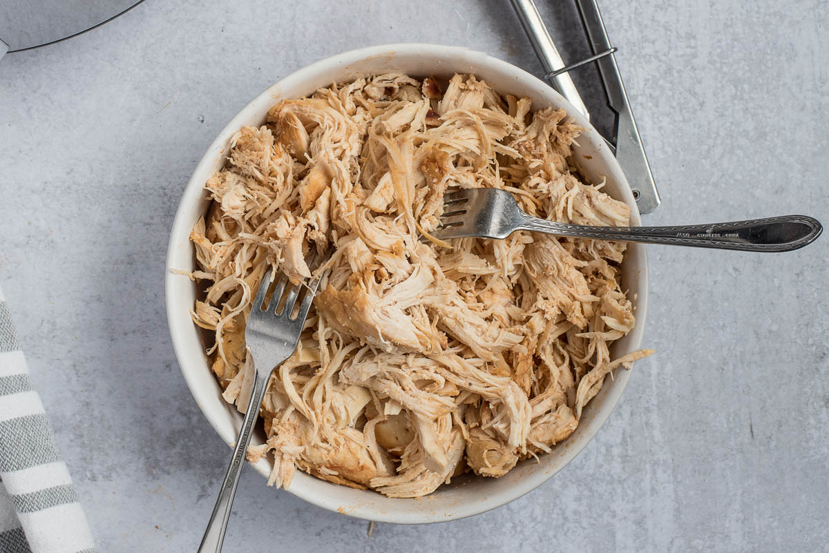 an overhead shot of chicken breasts in a bowl after having been shredded by two forks