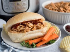 Pulled BBQ Chicken sandwich in front of an Instant Pot with carrots and potato chips plated in the foreground