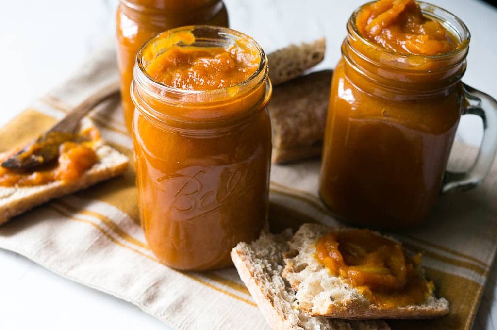 Pressure Cooker Spiced Pumpkin Apple Butter in glass jars, with the butter spread onto fresh bread next to them