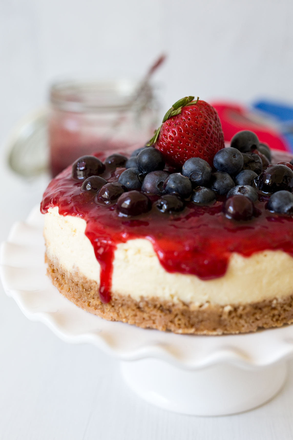 pressure cooker cheesecake with fresh blueberries and strawberry sauce on a white cake stand