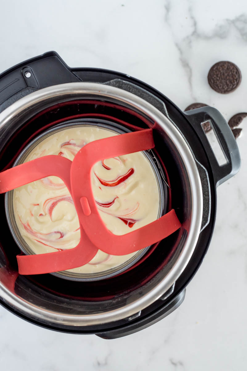 An overhead shot of an Instant Pot with the red velvet cheesecake inside the springform pan, resting on a trivet inside the cooking pot.