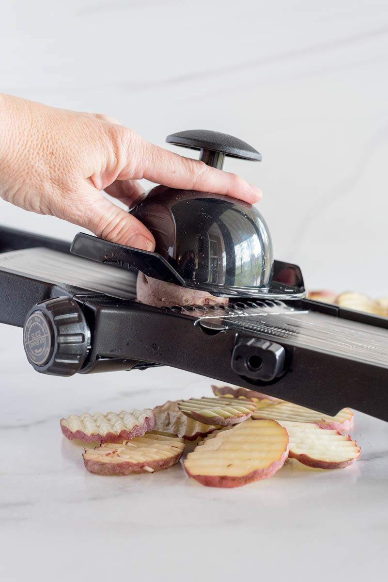 a side shot of a hand slicing red new potatoes with a mandoline