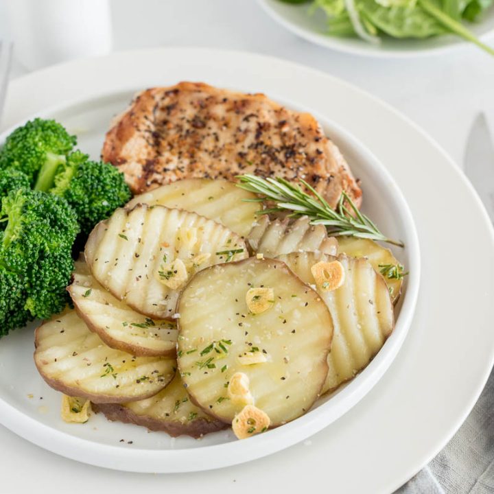 a small white plate with chicken and broccoli with the sliced new potatoes in the front, garnished with rosemary