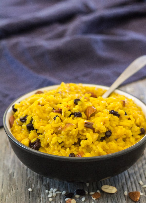 black serving bowl filled with bright yellow Saffron Risotto with Almonds and Currants 