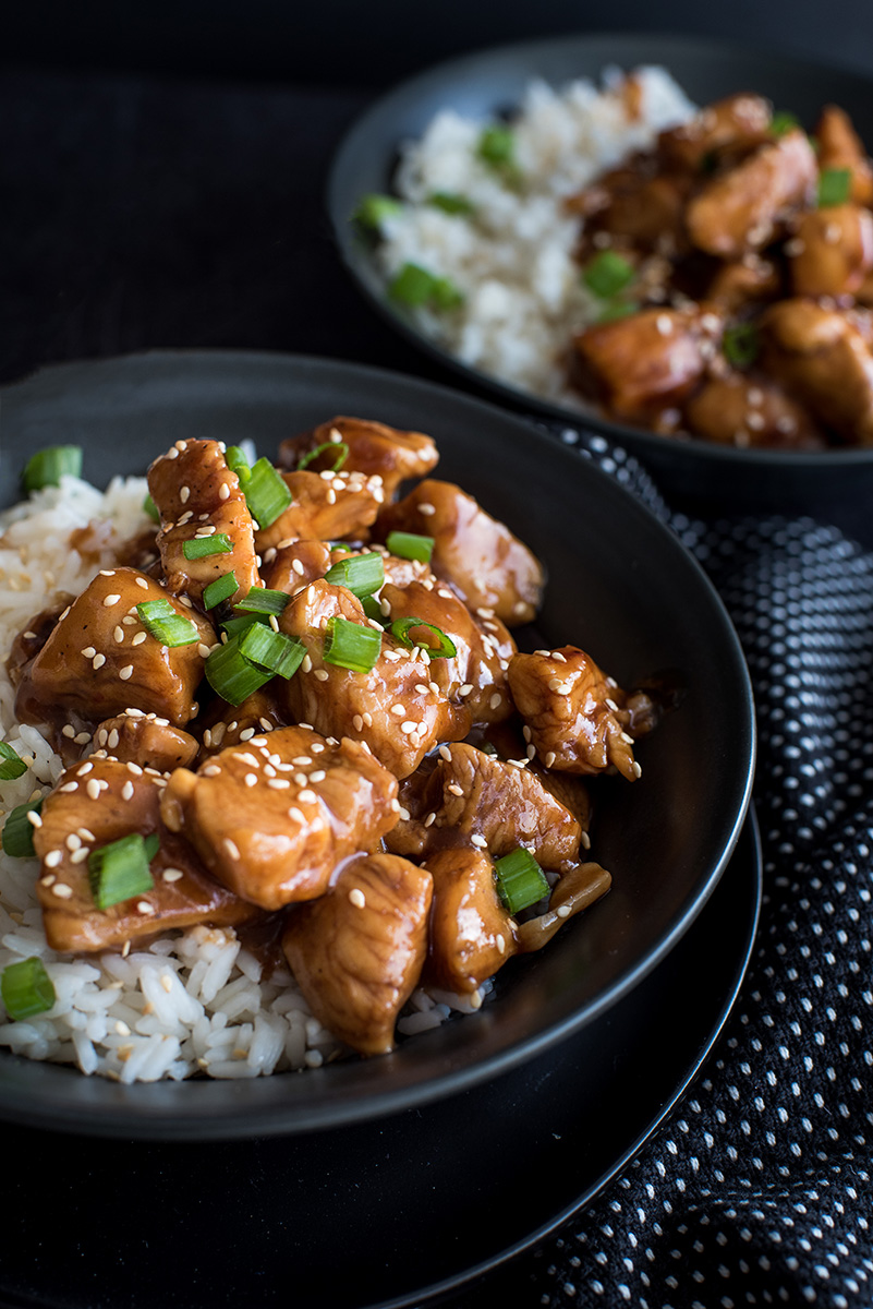 Close up on two bowls filled with Pressure Cooker white rice and Instant Pot Honey Sesame Chicken garnished with freshly cut green onions, white sesame seeds, and a sticky honey soy sauce.