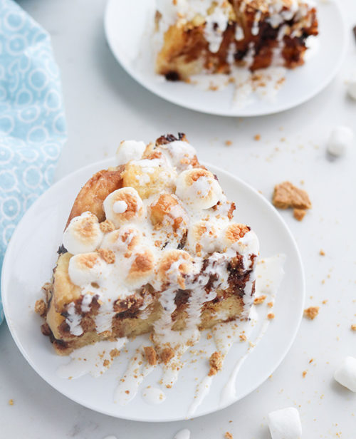 Smores bread pudding dished up on two plates, drizzled with marshmallow cream topping