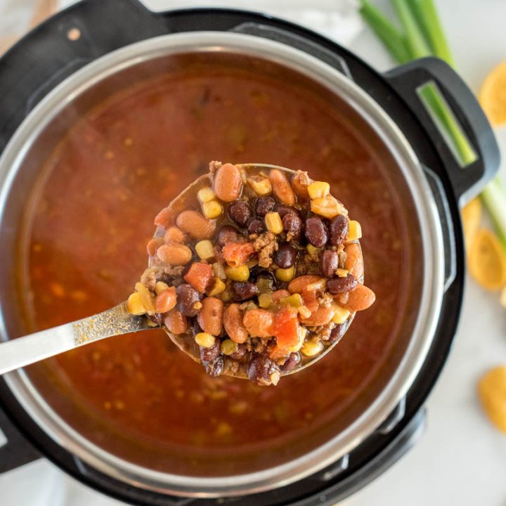 Overhead picture of an Instant Pot with taco soup cooked inside and a spoonful of diced tomatoes, beans, corn, and meat over the top.