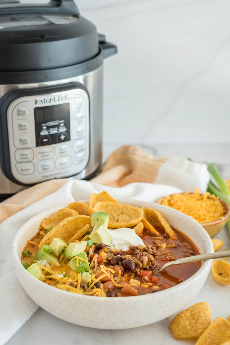 A bowl of taco soup topped with sour cream, cheese, avocado, and chips, placed in front of an Instant Pot.