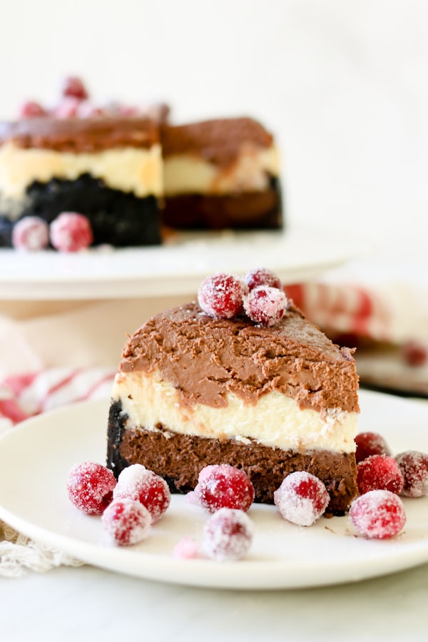 beautiful slice of Triple Chocolate Layered Cheesecake on a white plate. Cheesecake garnished with sugared cranberries.