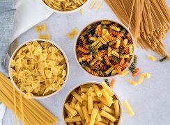 Overhead shot on three white bowls of pasta filled with bow ties, rotini, and penne pasta arranged in a triangular shape, with fettuccini and spaghetti in the corners