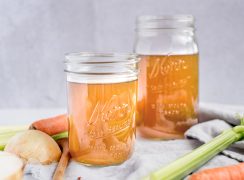 Two mason jars of vegetable stock made in the Instant Pot with celery and carrots on a gray napkin in the foreground
