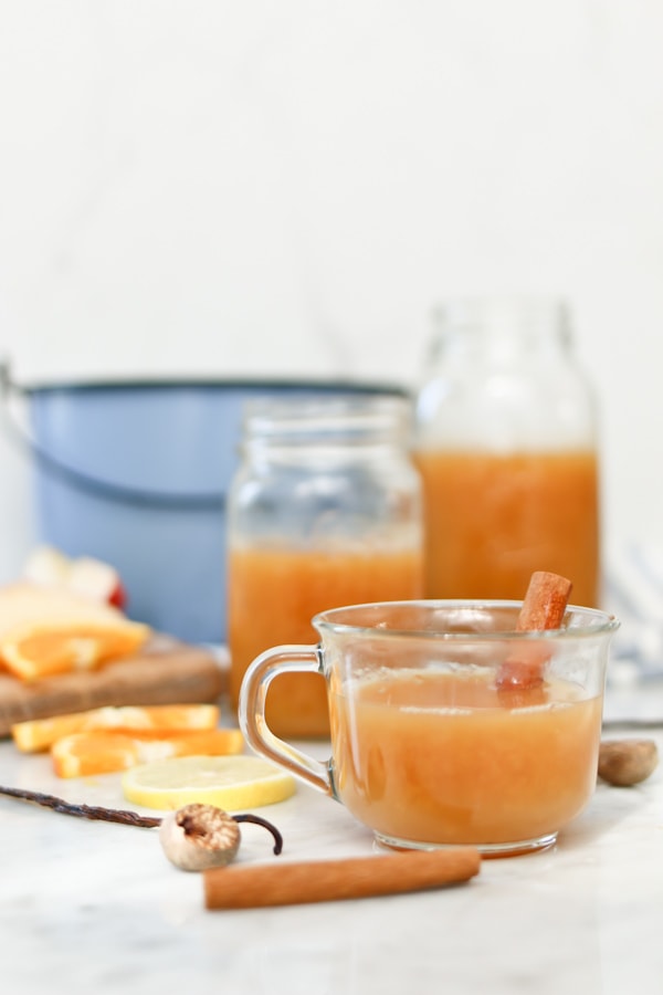 a batch of wassail made in an electric pressure cooker being served in clear coffee mugs with a cinnamon stick