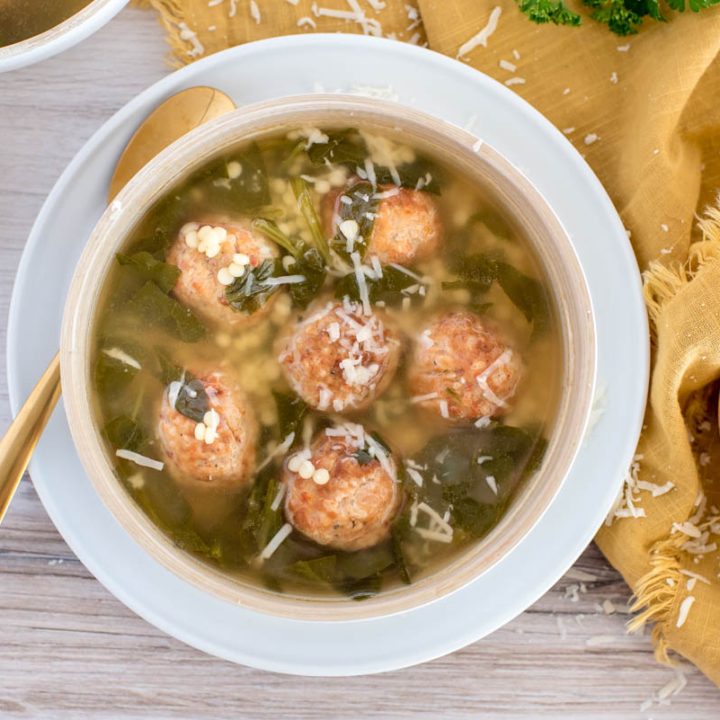 An overhead shot of Instant Pot Italian wedding soup in a white bowl, with fresh bread and grated parmesan cheese in the background.