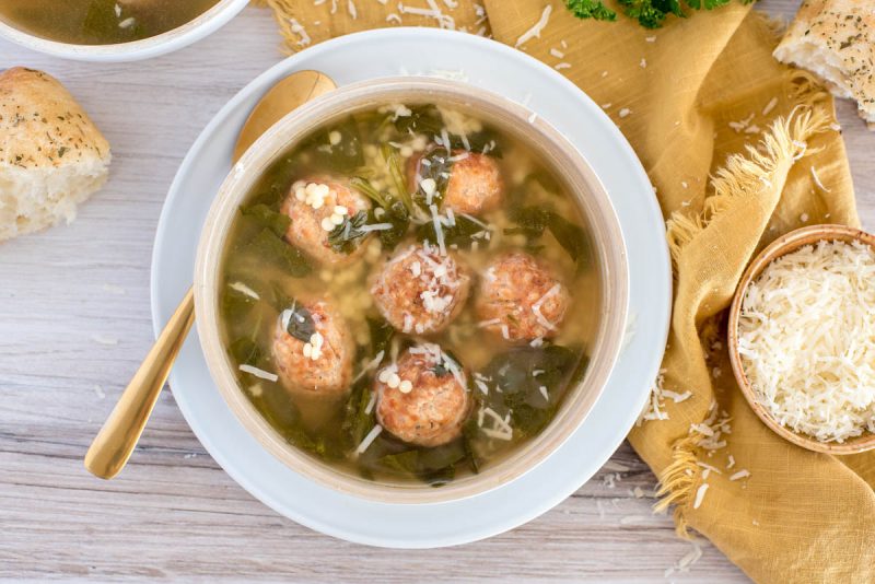An overhead shot of Instant Pot Italian wedding soup in a white bowl, with fresh bread and grated parmesan cheese in the background.
