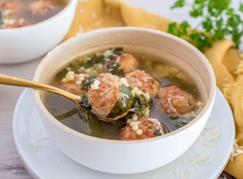 Close up picture of a white bowl with Instant Pot Italian wedding soup, placed on a yellow cloth with fresh parsley in the background.
