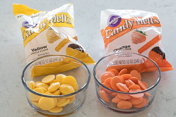 Orange and yellow candy melts in bowls with packages behind them